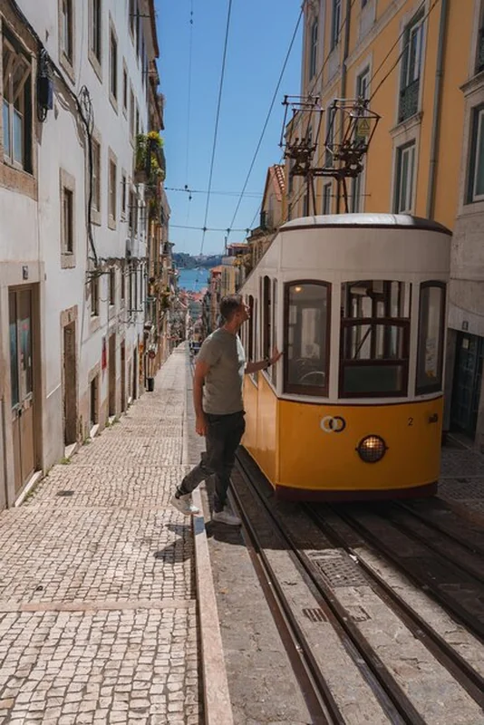 Historyczny żółty tramwaj na ulicy w Lizbonie z widokiem na rzekę Tagus
