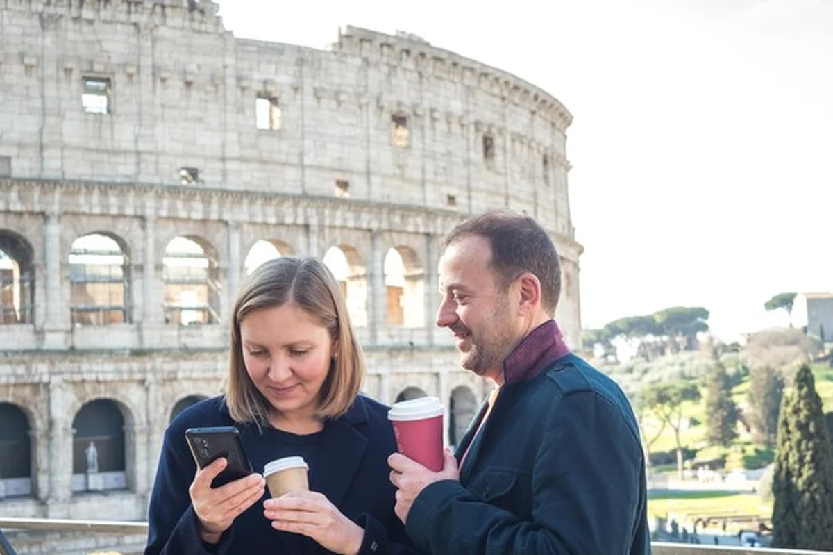 Para młodych ludzi pije kawę i korzysta z telefonu przed Koloseum w Rzymie